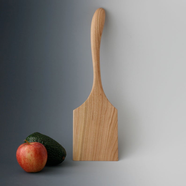 Cherry wood griddle spatula with rectangular blade and curved handle.