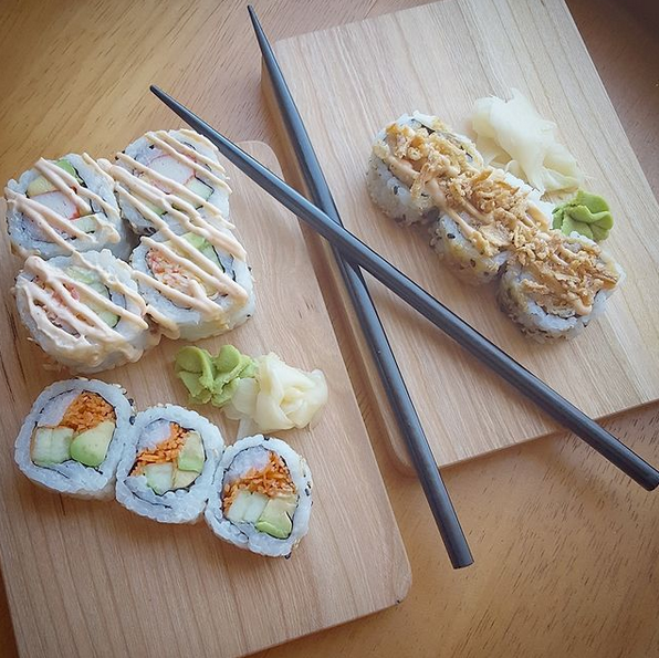 Small black cherry cutting boards used as sushi plates. Spicy rolls, wasabi, ginger, and tempura crumbles. Chopsticks.