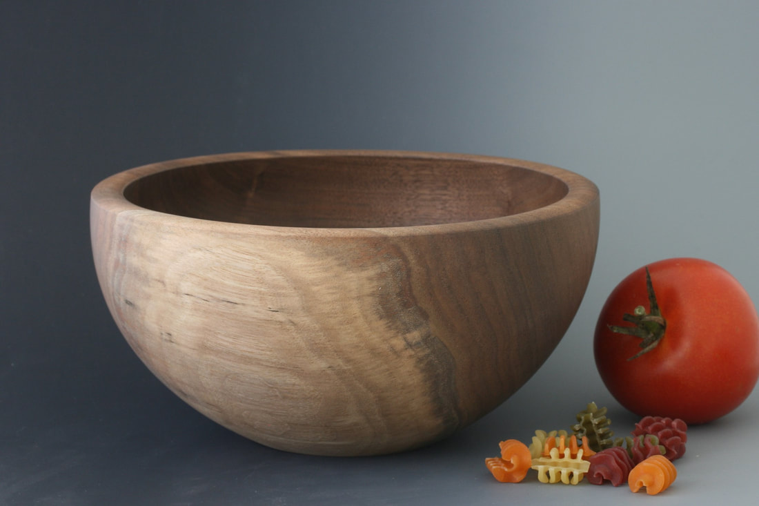 Black walnut wood bowl against a gray background and tricolor pasta and tomato for scale.