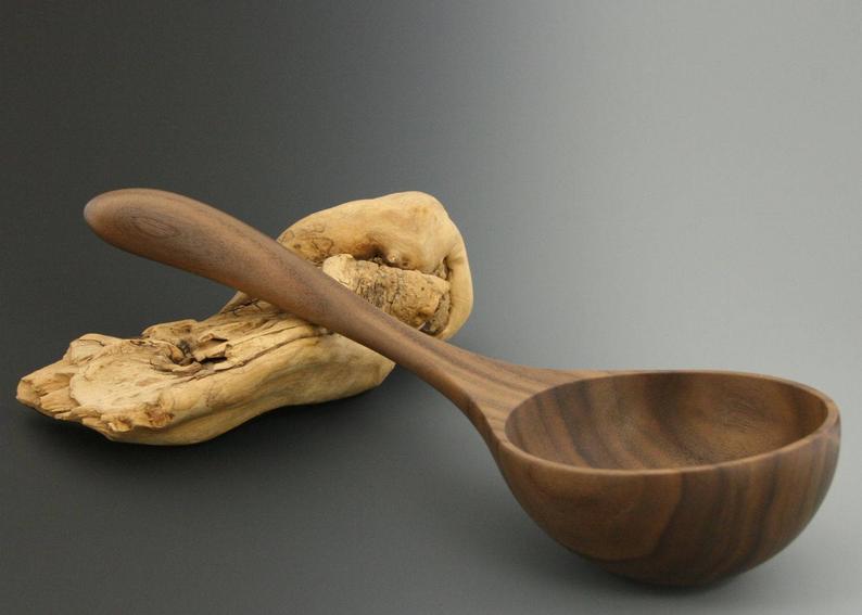 Black walnut wood serving ladle spoon with a deep bowl and short handle.