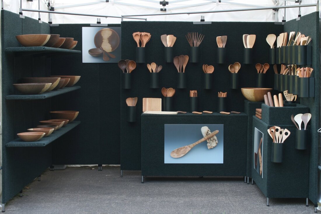 Juried art booth displaying handmade wooden bowls, boards, and kitchen and serving utensils.