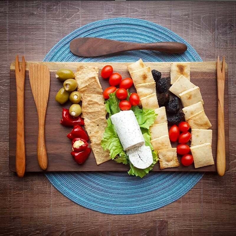 Black walnut cutting board used as a charcuterie board. Olive forks, french spatulas, and an assortment of crackers, cheese, and vegetables.