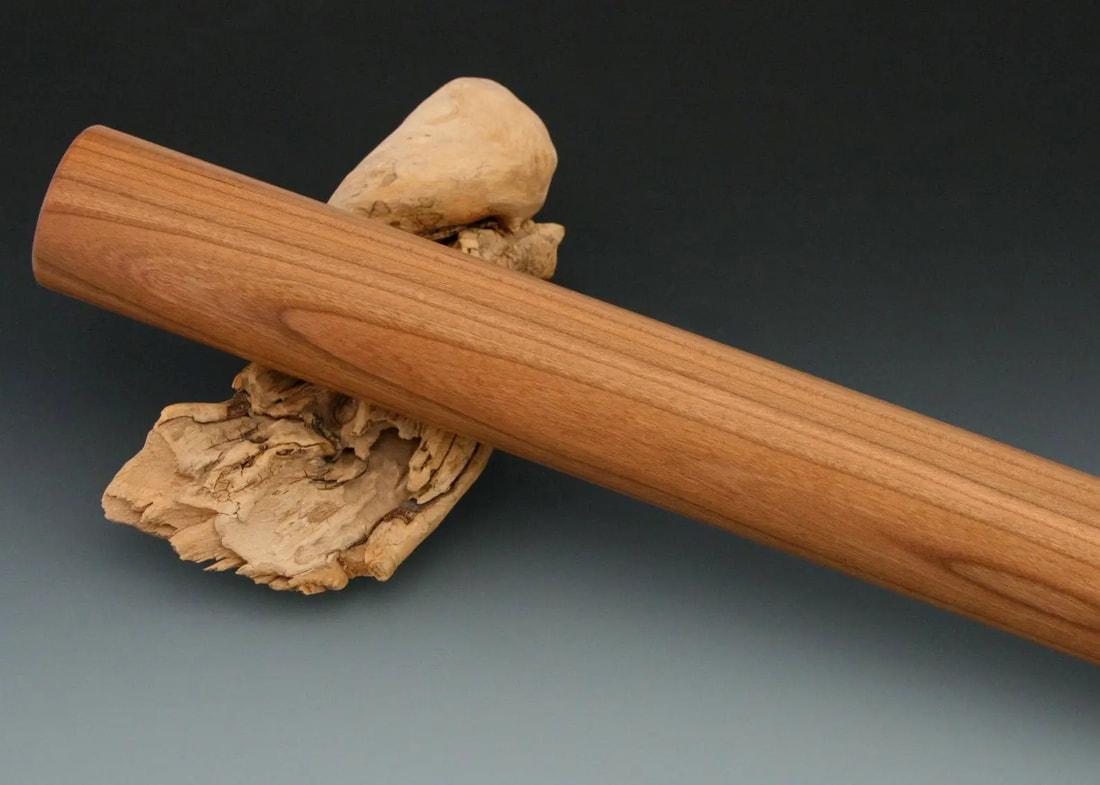 Close up of a straight cherry wood rolling pin on a gray gradient background and resting on a driftwood prop.