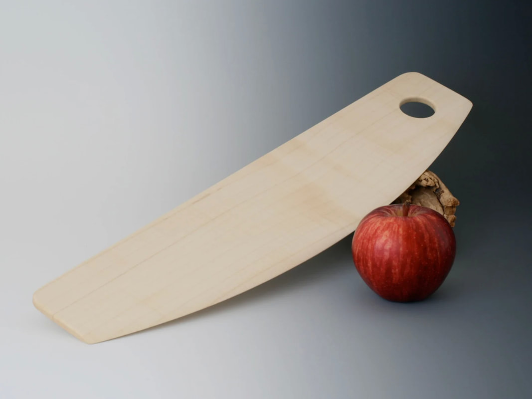 Rocker-style pizza cutter, handmade in maple wood with an apple for scale and on a gray gradient background.