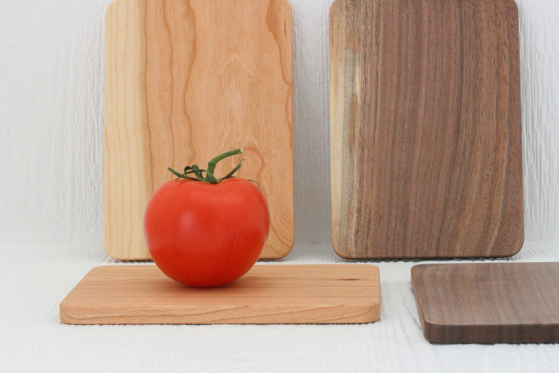 Four small cherry and walnut wood cutting boards, photographed on a white textured background and with a tomato for size.