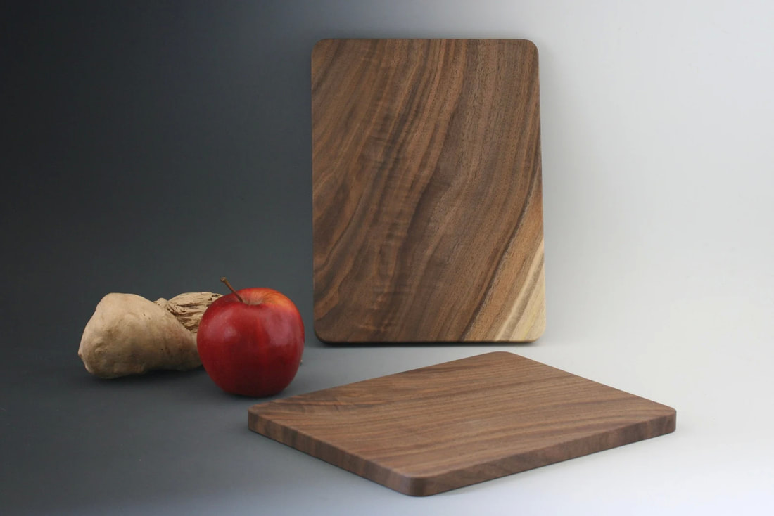 Small walnut wood cutting boards on a gray background and with an apple and driftwood prop for scale.