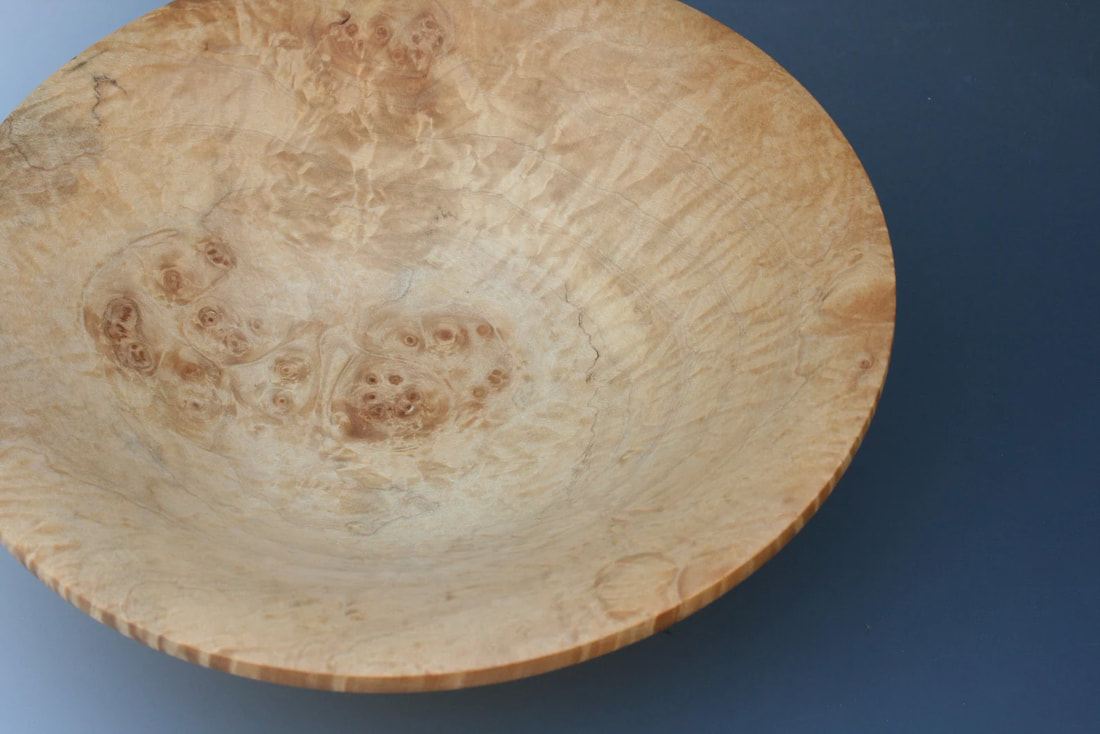 Close up of a maple bowl with burl inclusions on a gradient blue background.