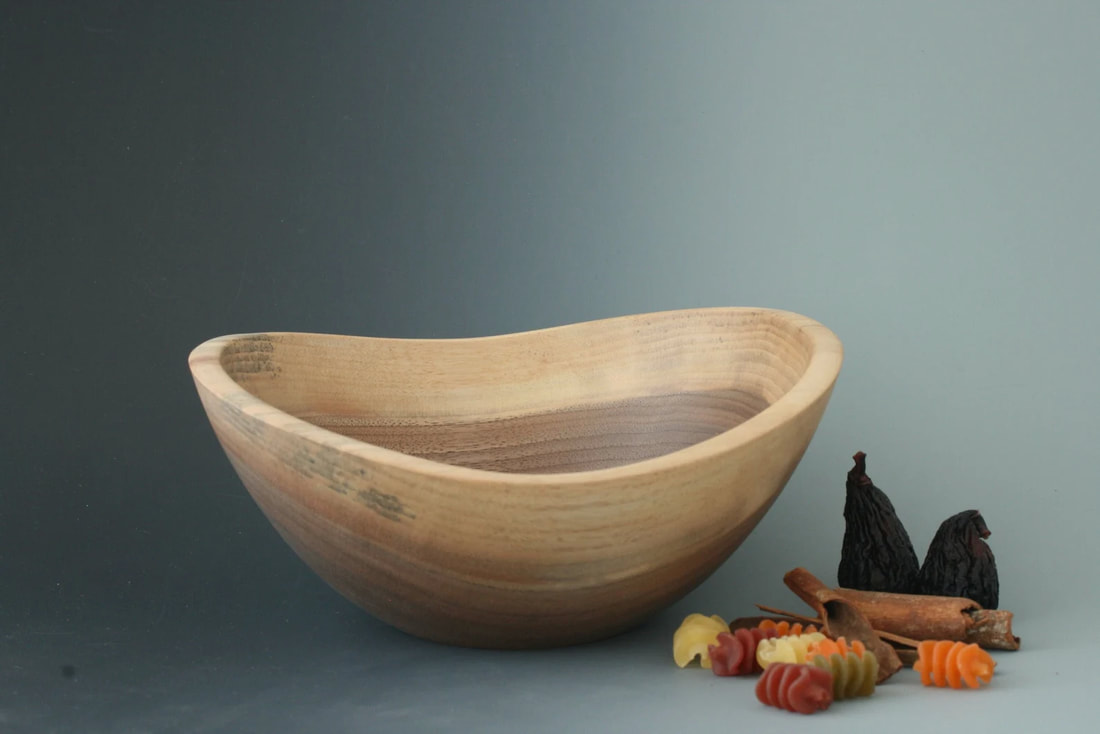 Walnut wood live edge functional art bowl on a gray background with figs, pasta, and cinnamon sticks for scale.