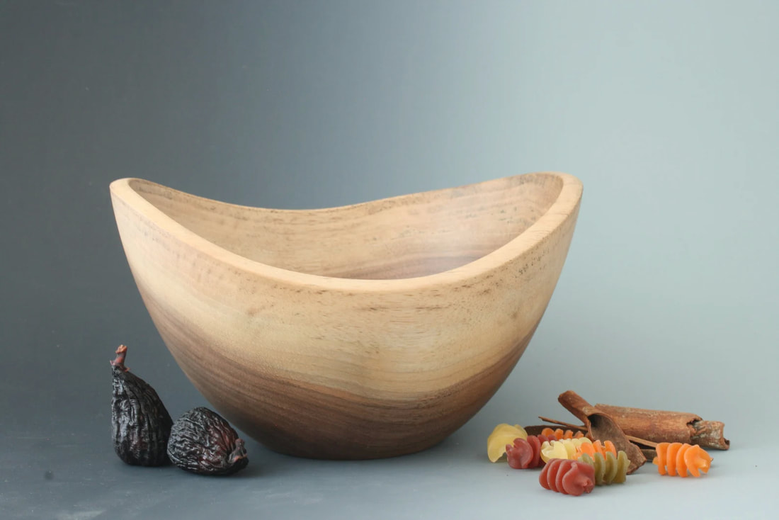 Black walnut wood live edge functional art bowl on a gray background with figs, pasta, and cinnamon sticks for scale.