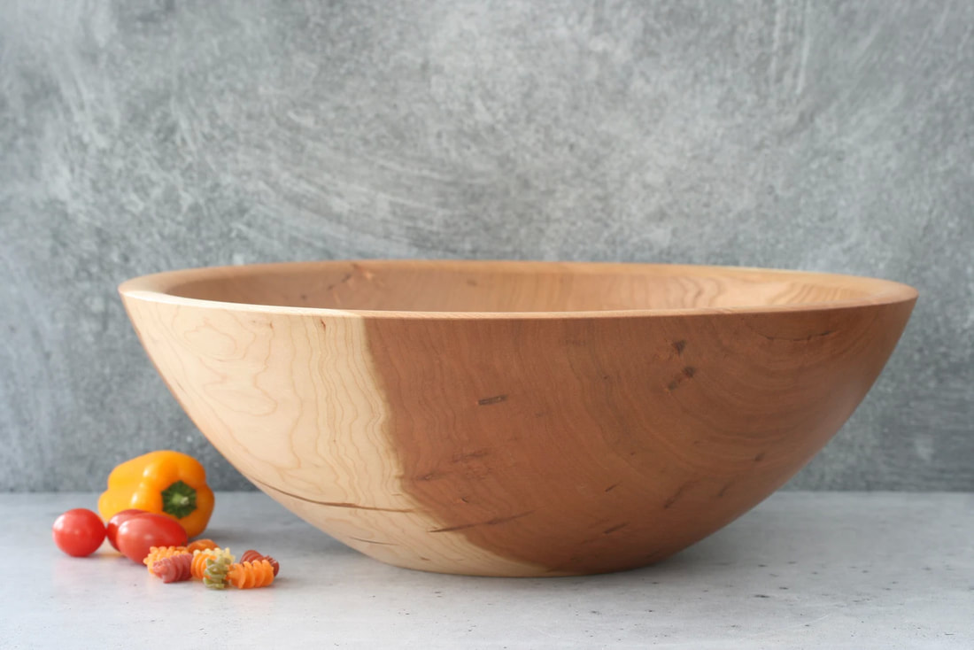 Large salad bowl on a gray countertop with a mini pepper, grape tomatoes, and dried pasta for scale.