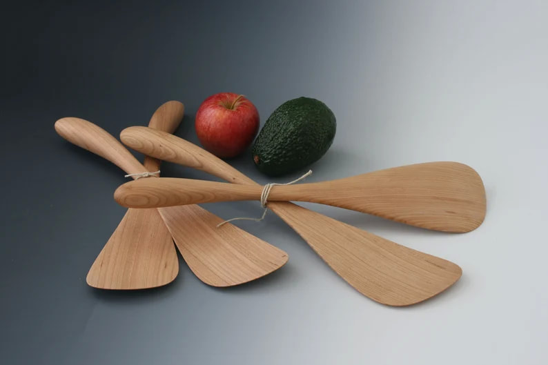 Cherry wood salad serving paddle pairs in two sizes on a gray gradient background with an avocado and apple for scale.