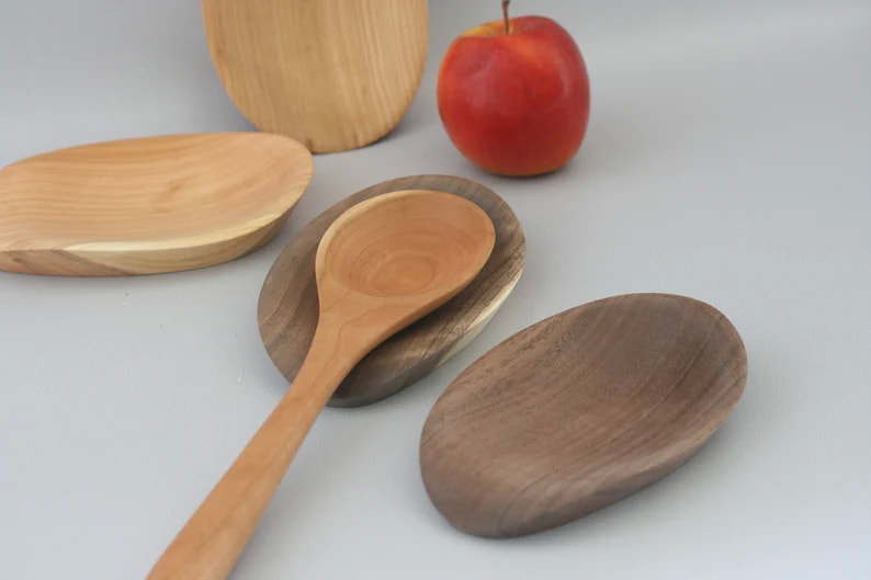 Handmade wooden spoon rests with a spoon and apple for scale. 