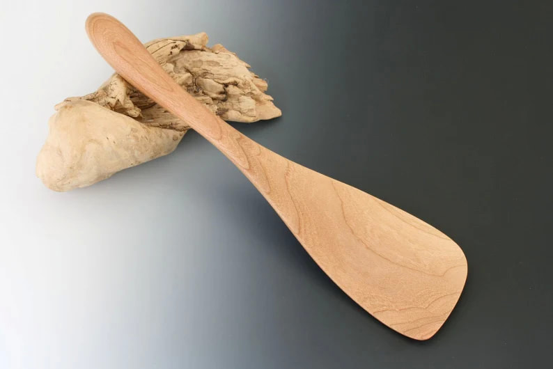 Cherry wood serving paddle on a gradient gray background and resting on a drift wood prop.