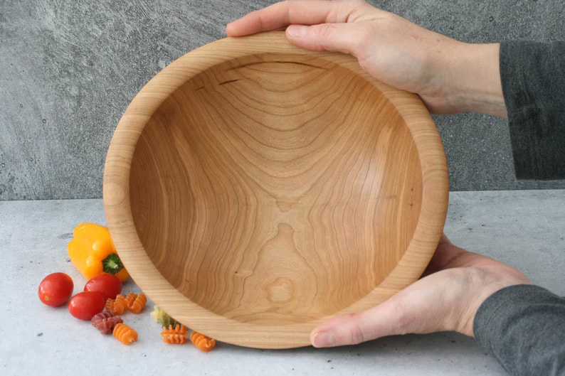 9 inch cherry wood bowl shown against a gray background and with peppers, cherry tomatoes, and dried pasta for scale.