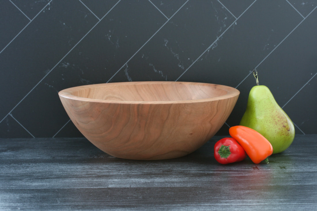 Handmade cherry wood bowl on a dark gray barnwood coutertop and black marble backsplash, shown with a pear and mini peppers for scale.