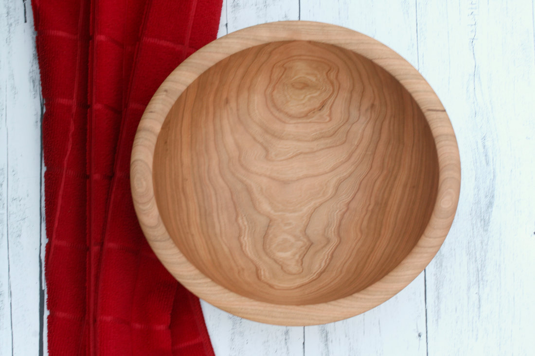 Cherry wood bowl on whitewashed countertop and red kitchen towel.