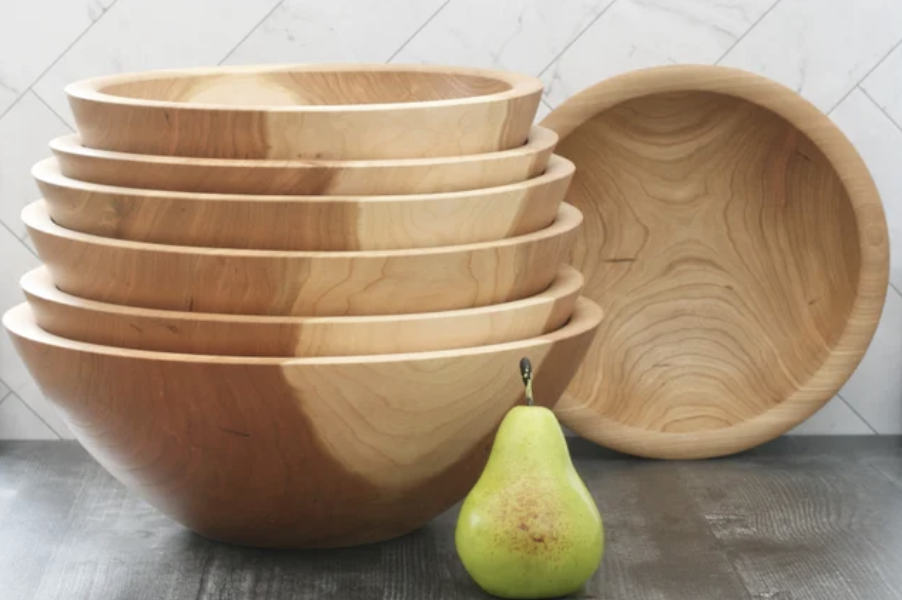 Stacked cherry wood turned salad bowls on a gray distressed table top, white marble backdrop, and a green pear for scale.